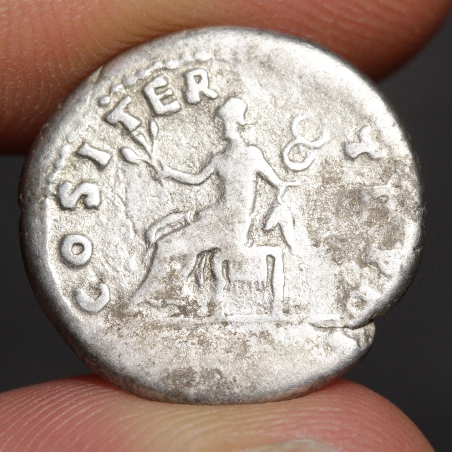 Ancient silver coin held between fingers with 'COSTIER' engraved