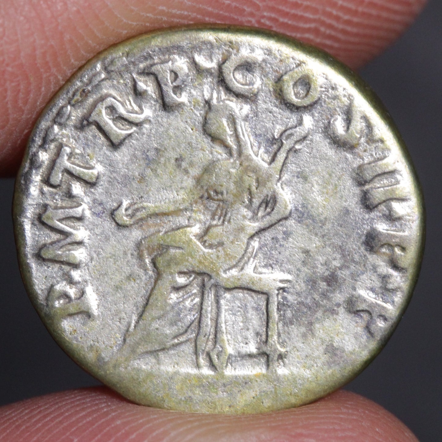 Ancient coin with engraved figure and text held between fingers