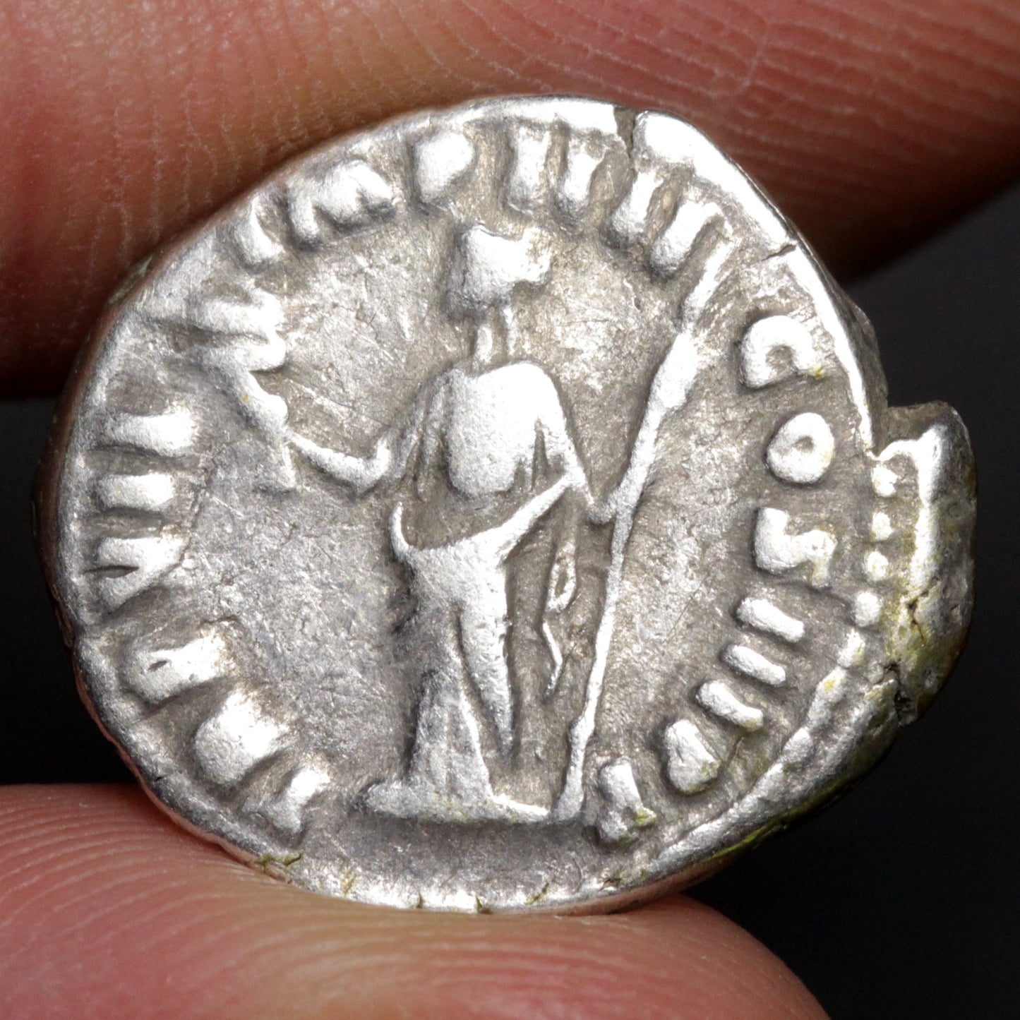 Ancient silver coin held between fingers with detailed design