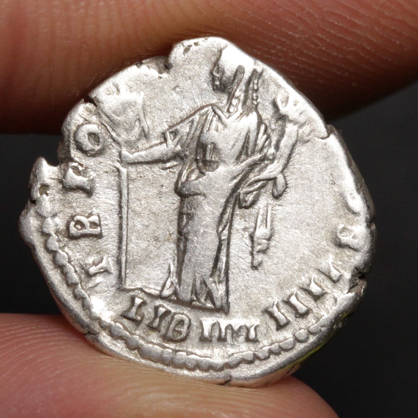 Ancient silver coin held between fingers with dark background