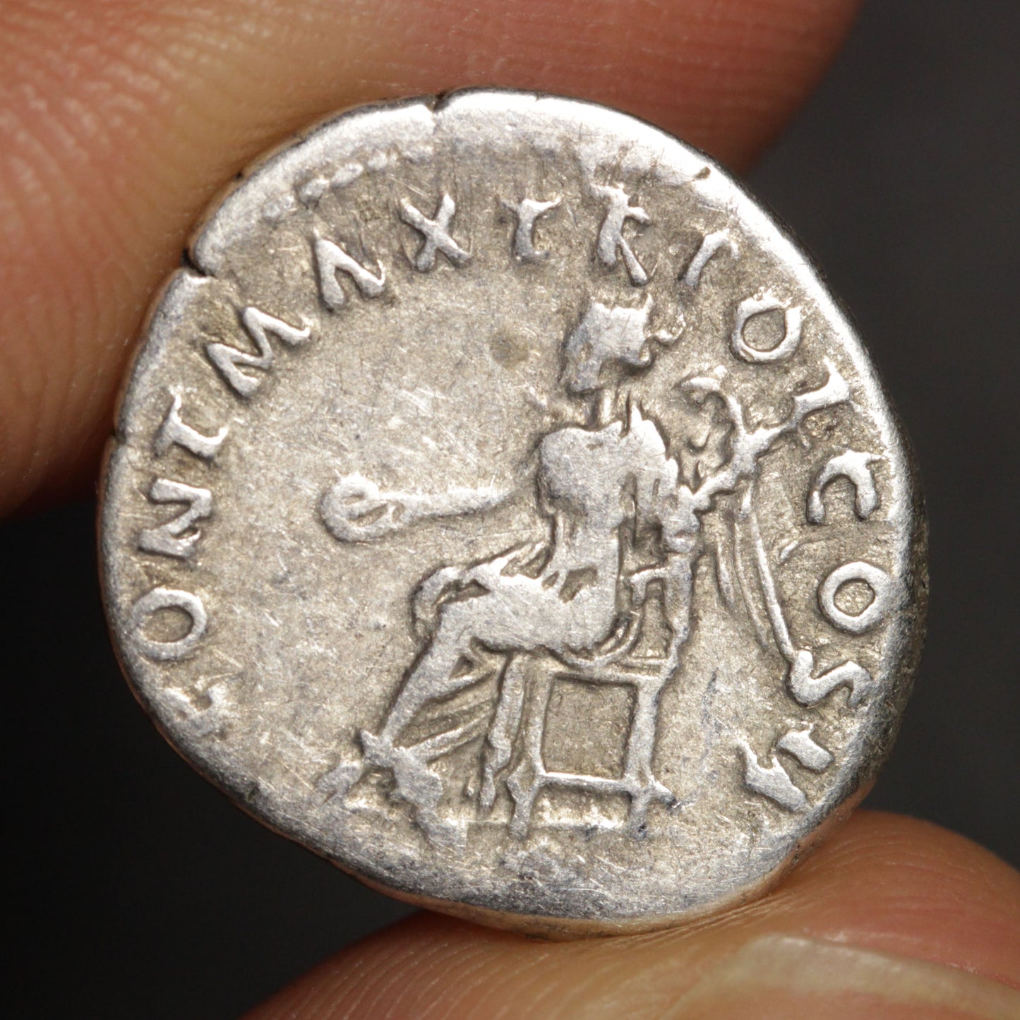 Ancient silver coin held between fingers with detailed engravings