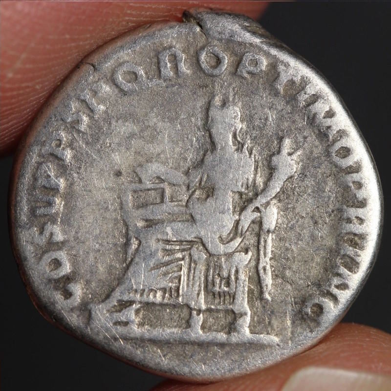 Ancient Roman silver coin held between fingers with dark background