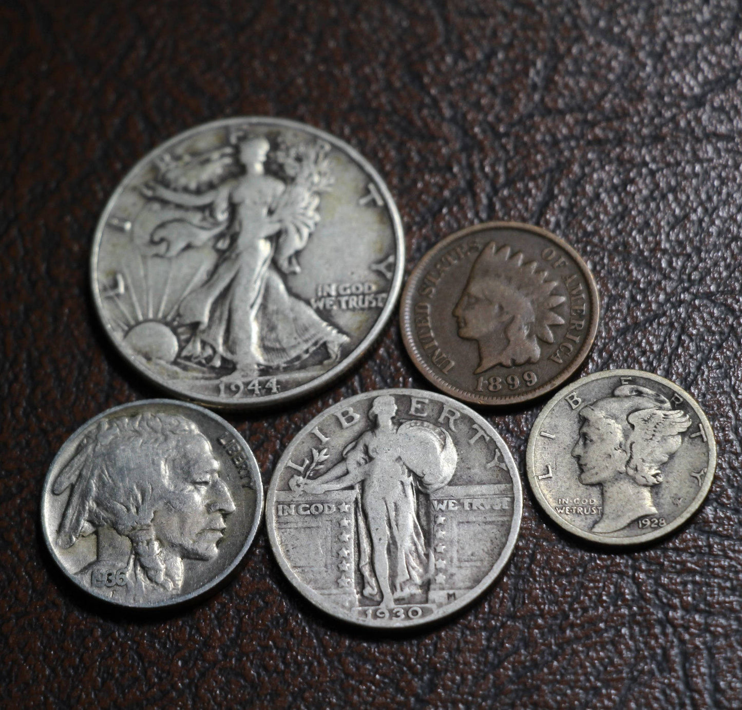 The obverse side of five old American coins next to each other, including a Walking Liberty half dollar, Standing Liberty quarter, Mercury dime, Buffalo nickel, and Indian head cent.