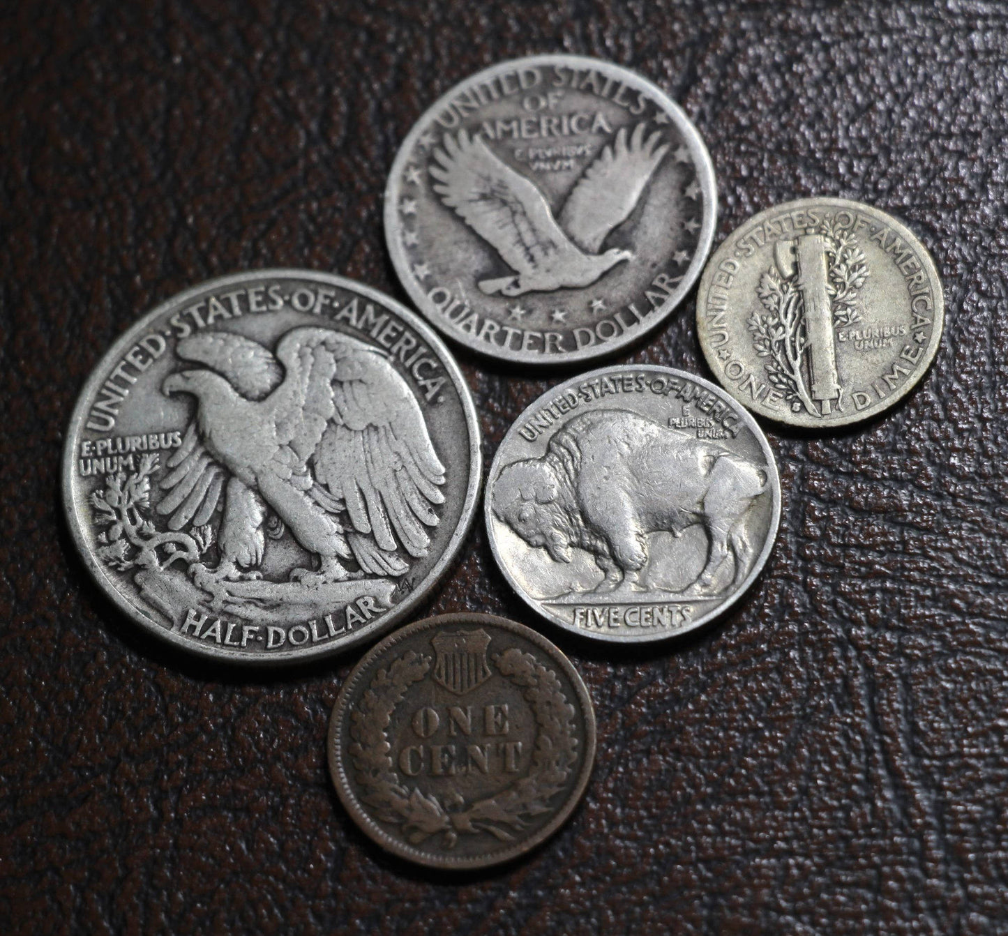 The reverse side of five old American coins next to each other, including a Walking Liberty half dollar, Standing Liberty quarter, Mercury dime, Buffalo nickel, and Indian head cent.
