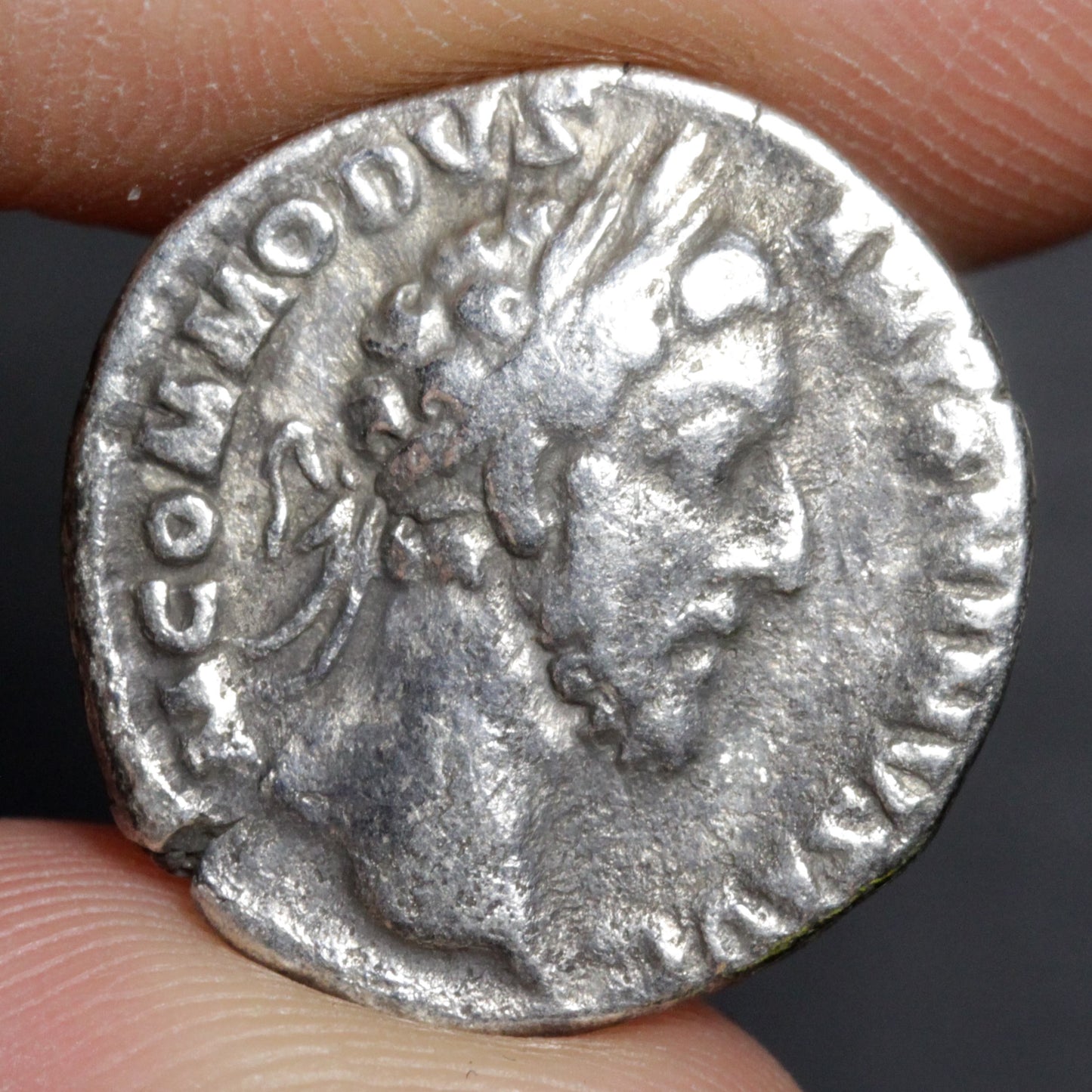 Silver ancient coin with profile of a person held between fingers against a dark background