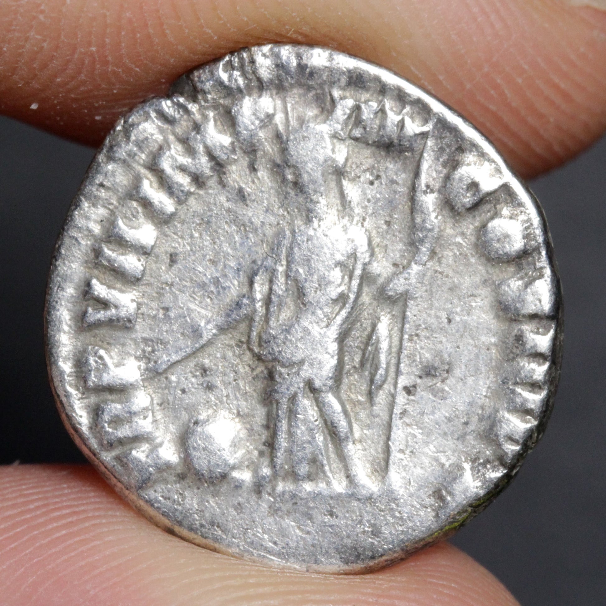 Silver Roman coin held between fingers with a dark background
