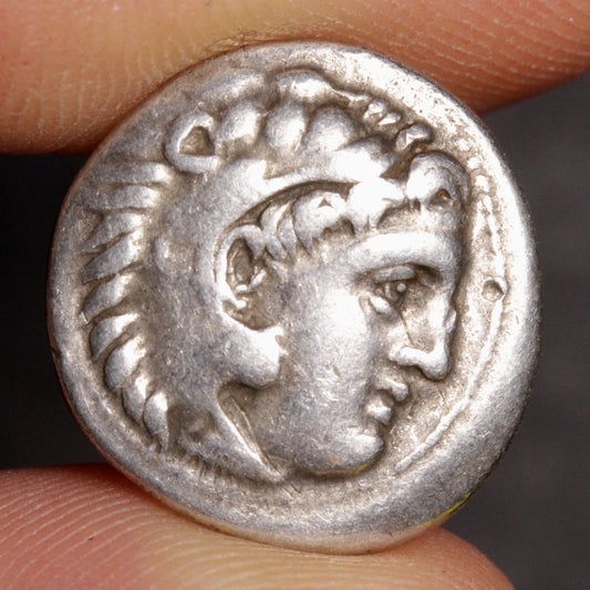 Silver coin with a profile of a person held between fingers against a dark background