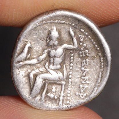 Ancient silver coin with engraved design held between fingers