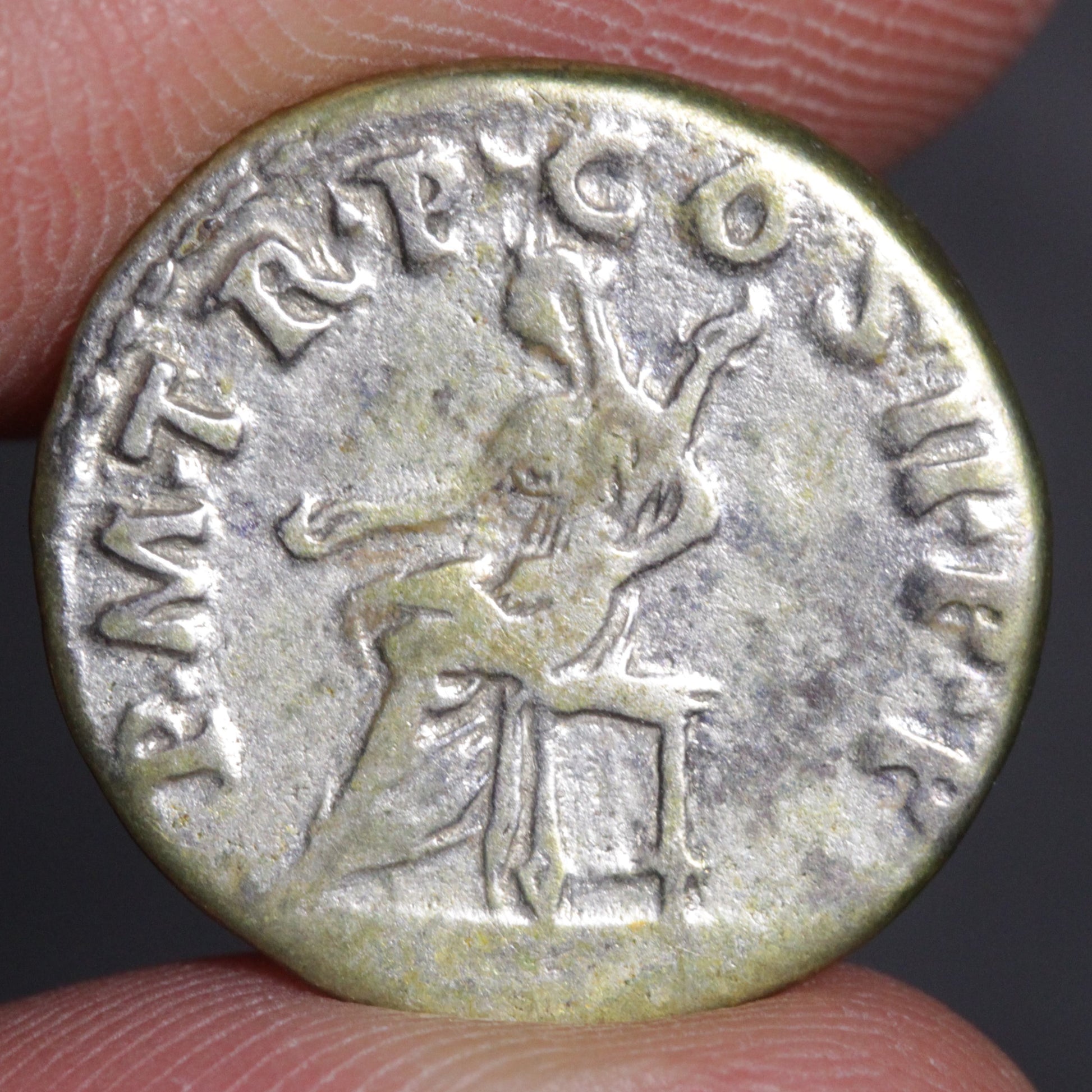 Ancient coin with engraved figure and text held between fingers