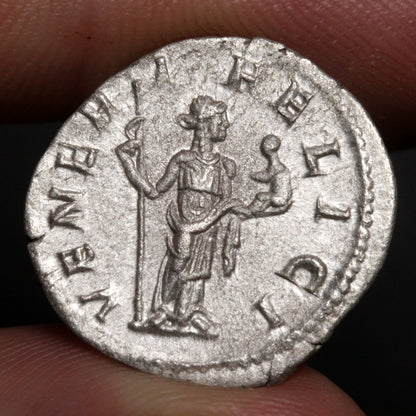 ancient roman coin being held between two fingers, design of venus holding cupid