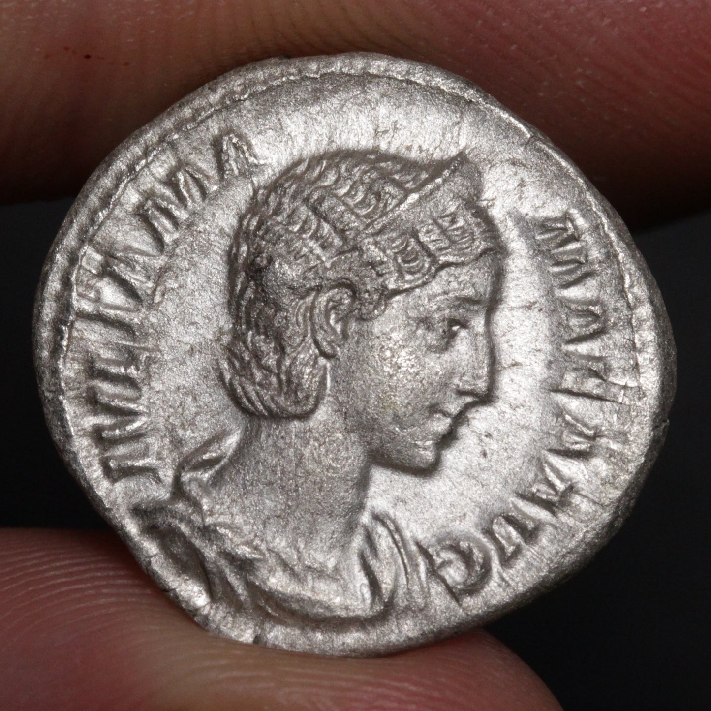 ancient roman coin being held between two fingers