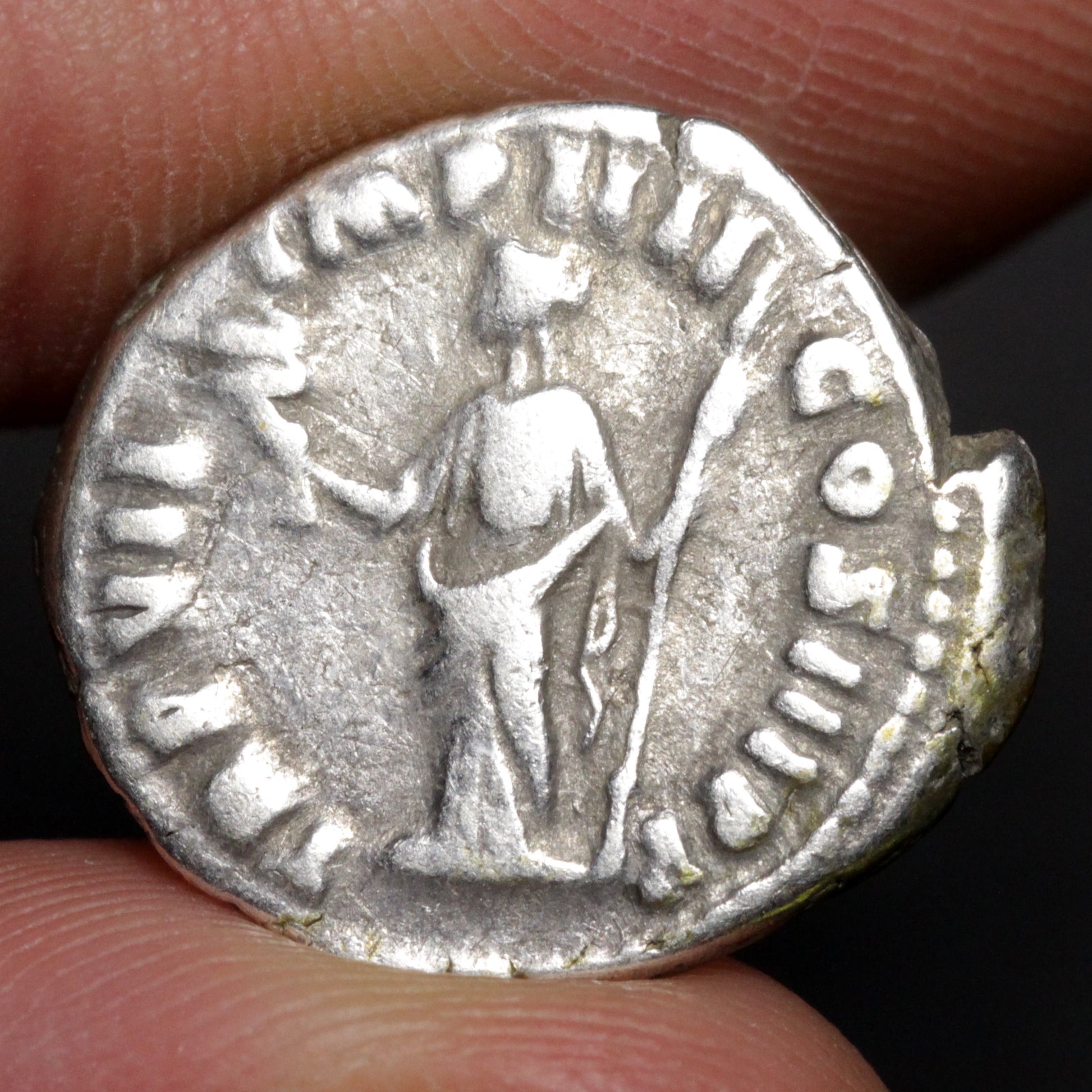 Ancient silver coin held between fingers with detailed design