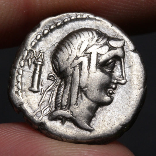 Ancient coin with a profile of a person and a candle, held between fingers.