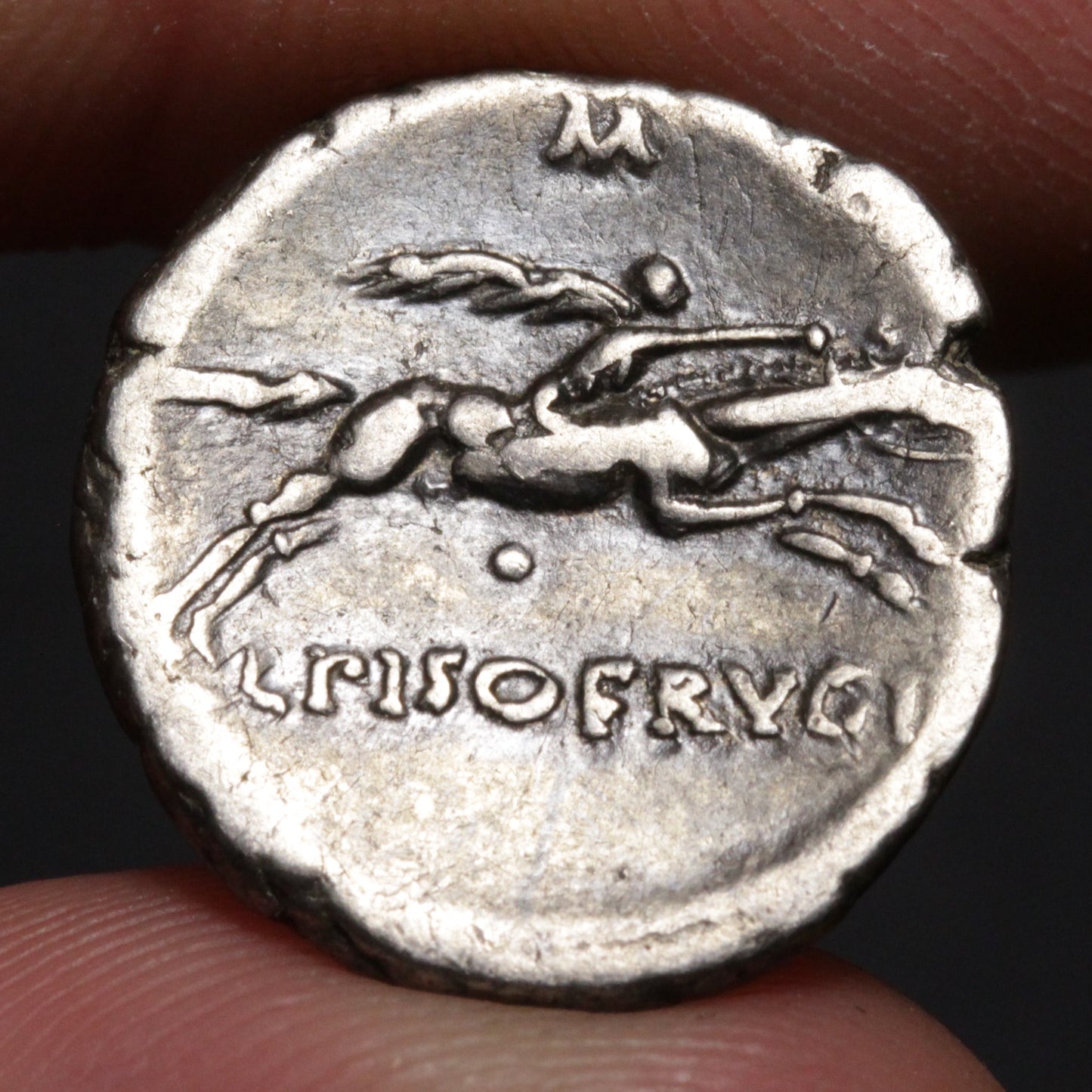Ancient coin with a horserider design and engraved text held between fingers.