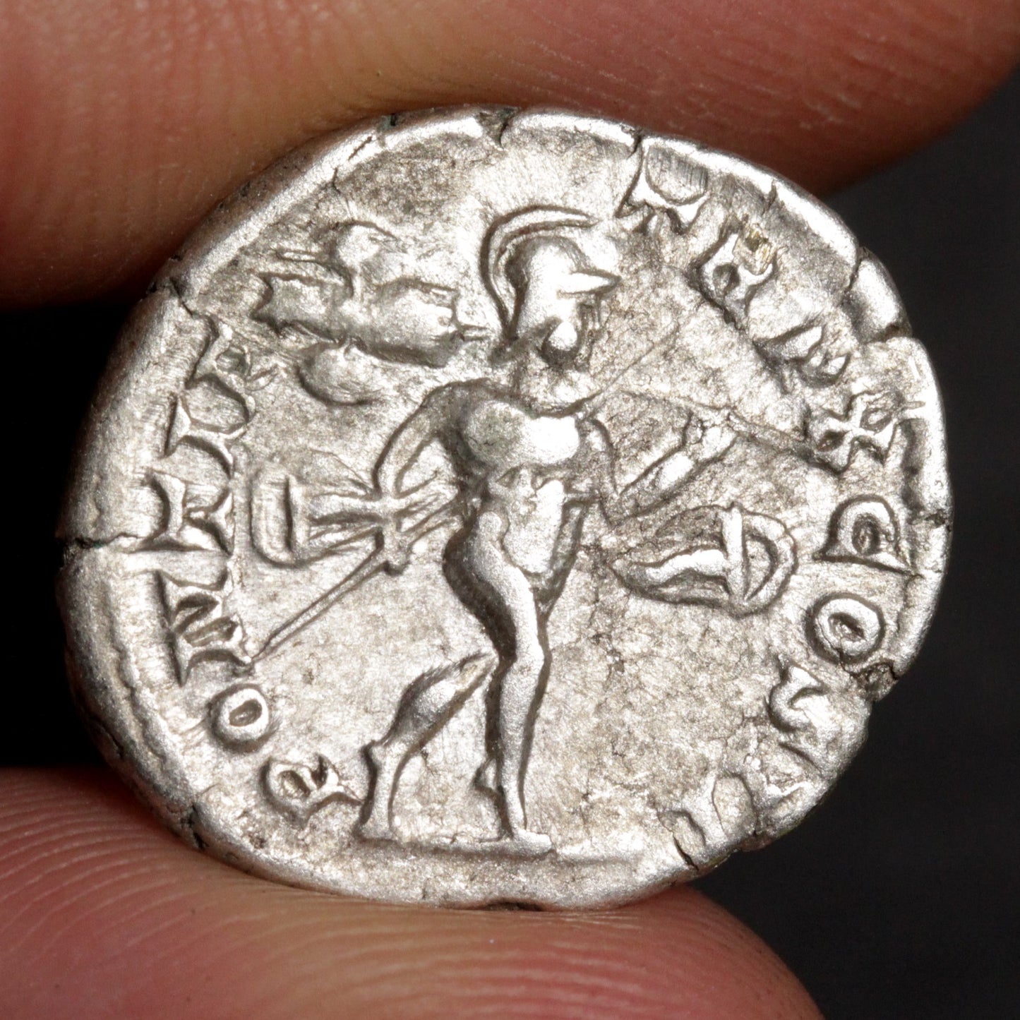 Ancient silver coin with a warrior figure held between fingers