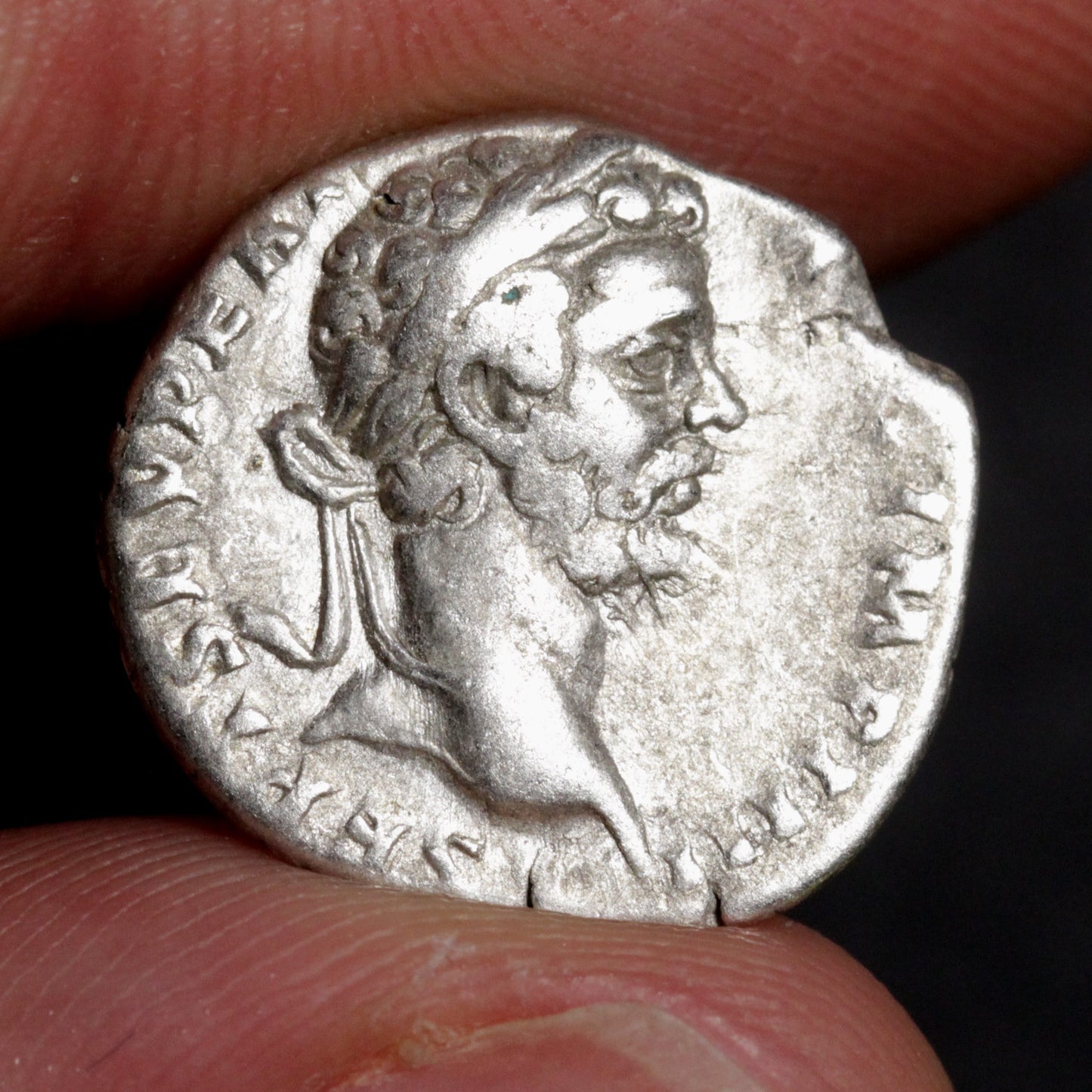 Ancient silver coin with a portrait held between fingers against a dark background