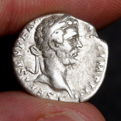 Ancient silver coin with a portrait held between fingers against a dark background