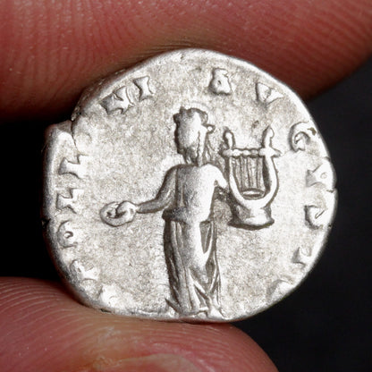 Ancient silver coin held between fingers with a dark background