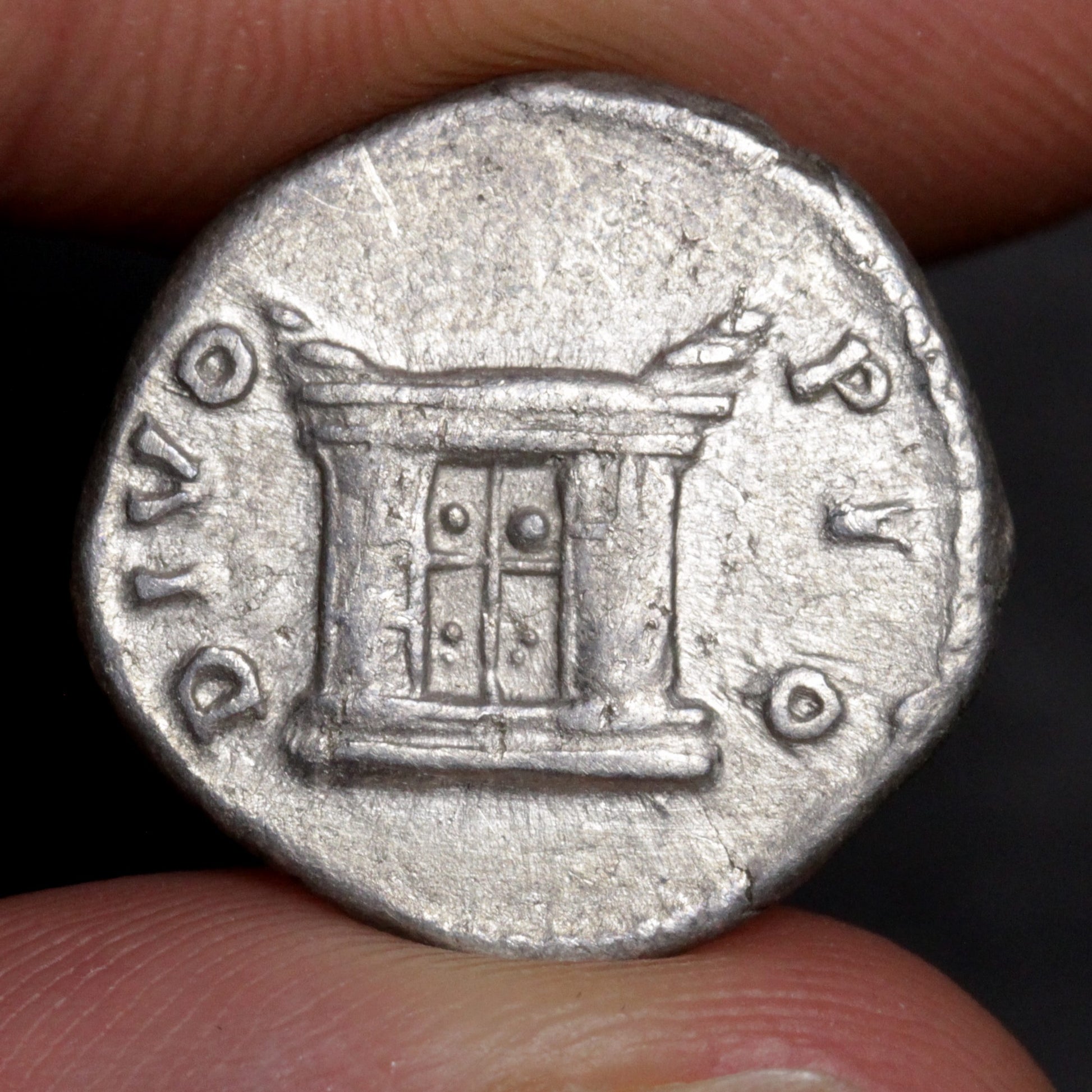 Ancient coin with architectural design held between fingers against a dark background