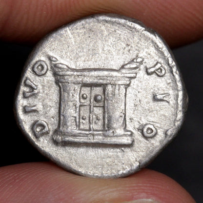 Ancient coin with architectural design held between fingers against a dark background