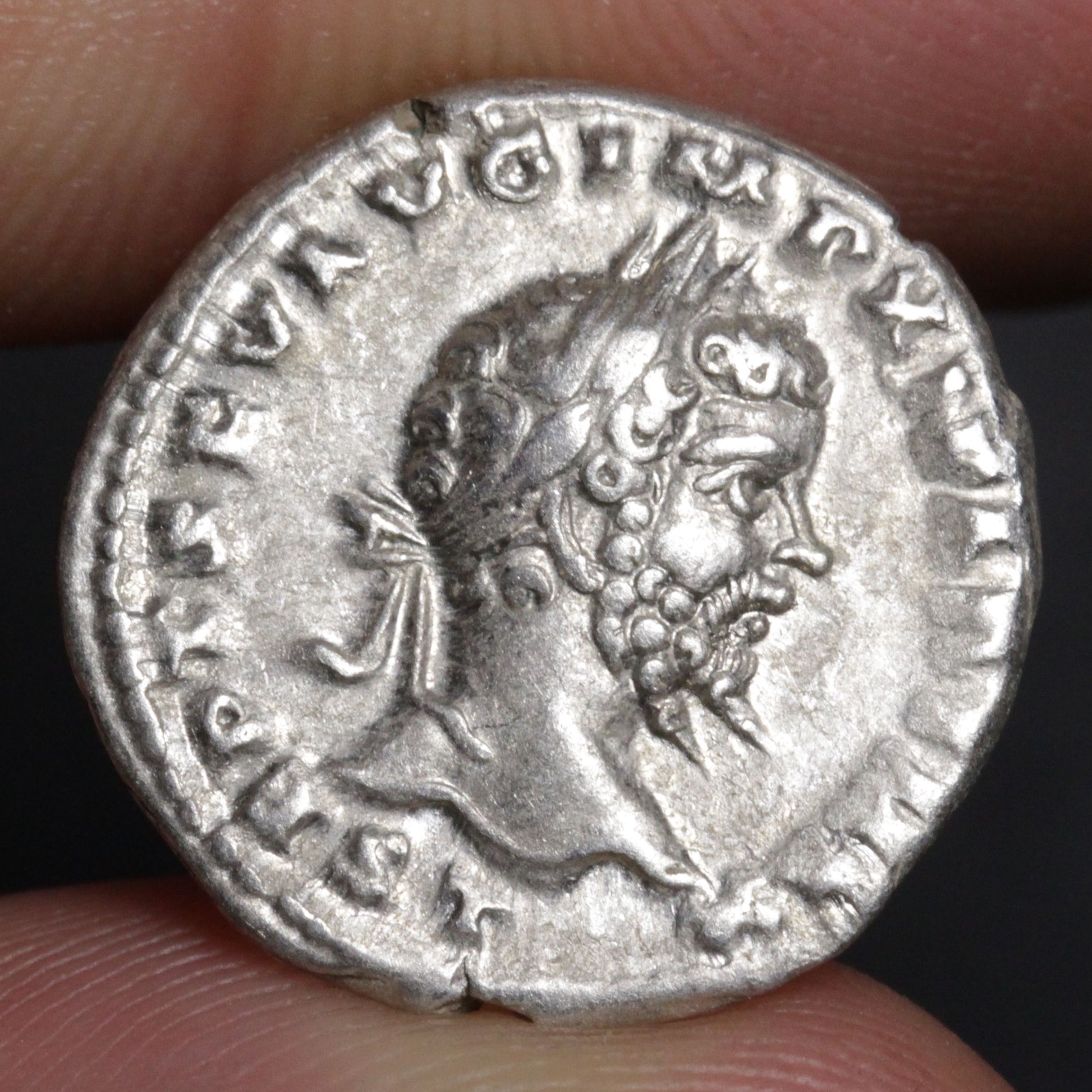 Ancient silver coin with a profile of a bearded man held between fingers