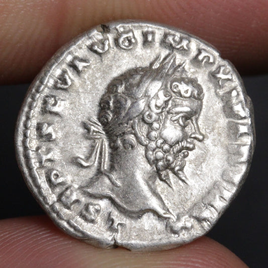 Ancient silver coin with a profile of a bearded man held between fingers