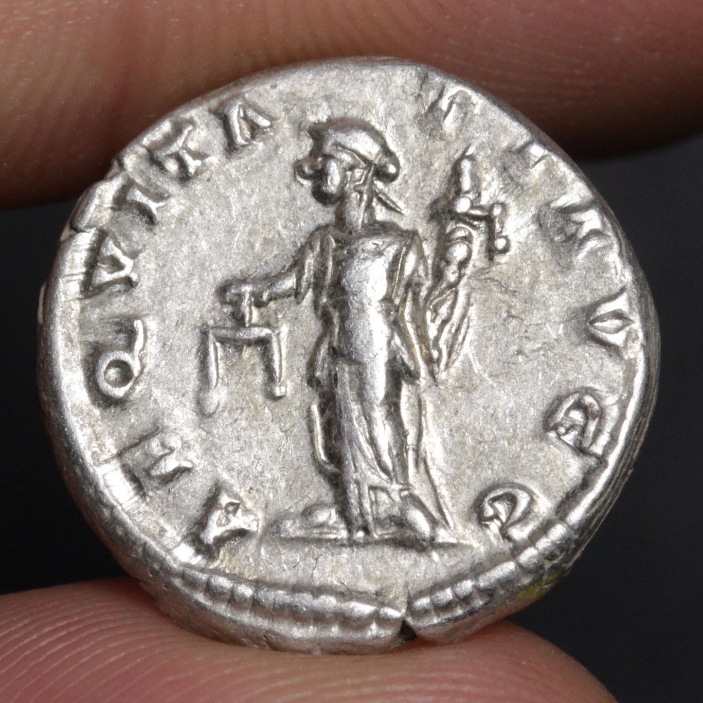 Silver Roman coin held between fingers with a dark background
