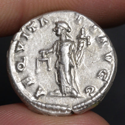 Silver Roman coin held between fingers with a dark background