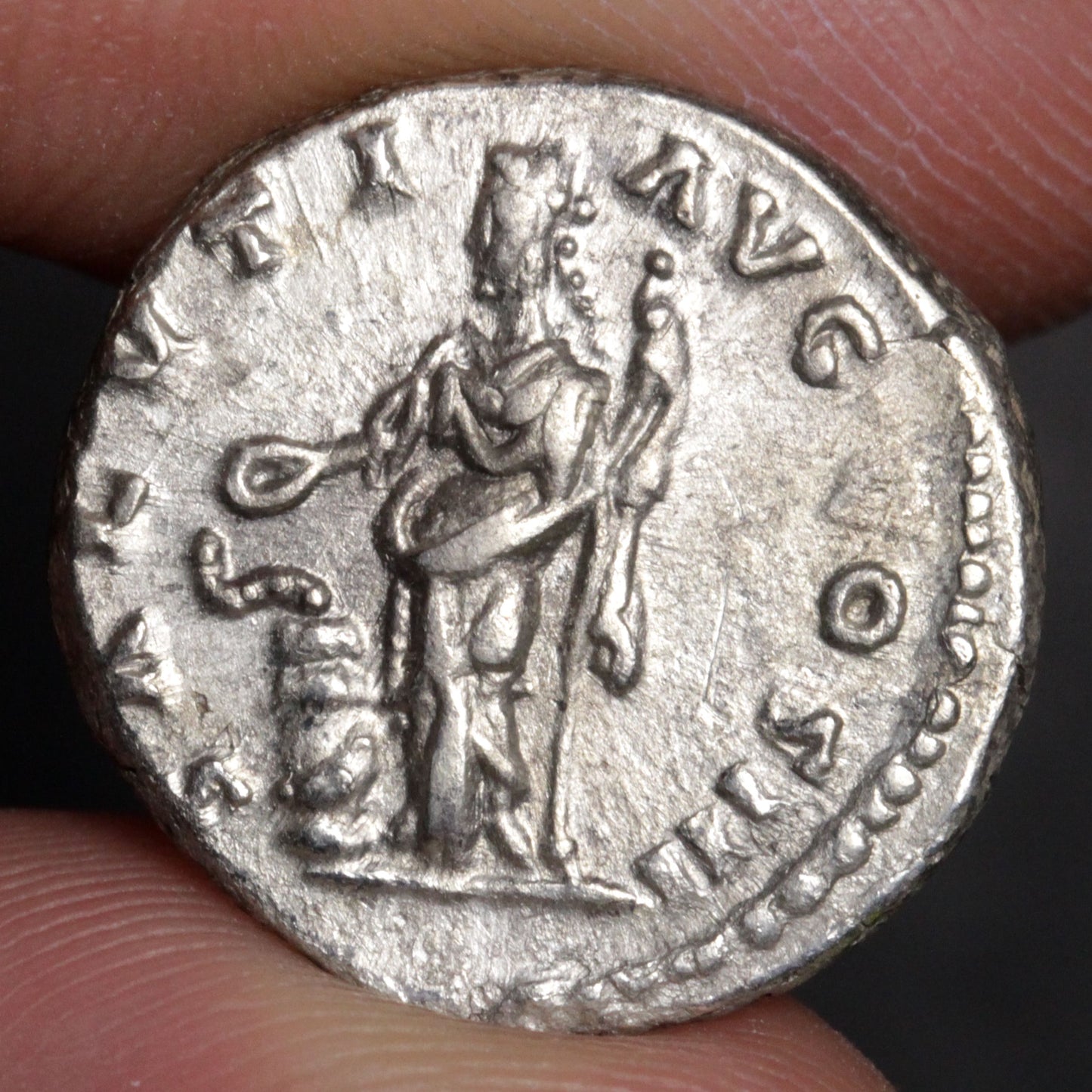 Ancient silver coin with a figure and inscriptions held between fingers