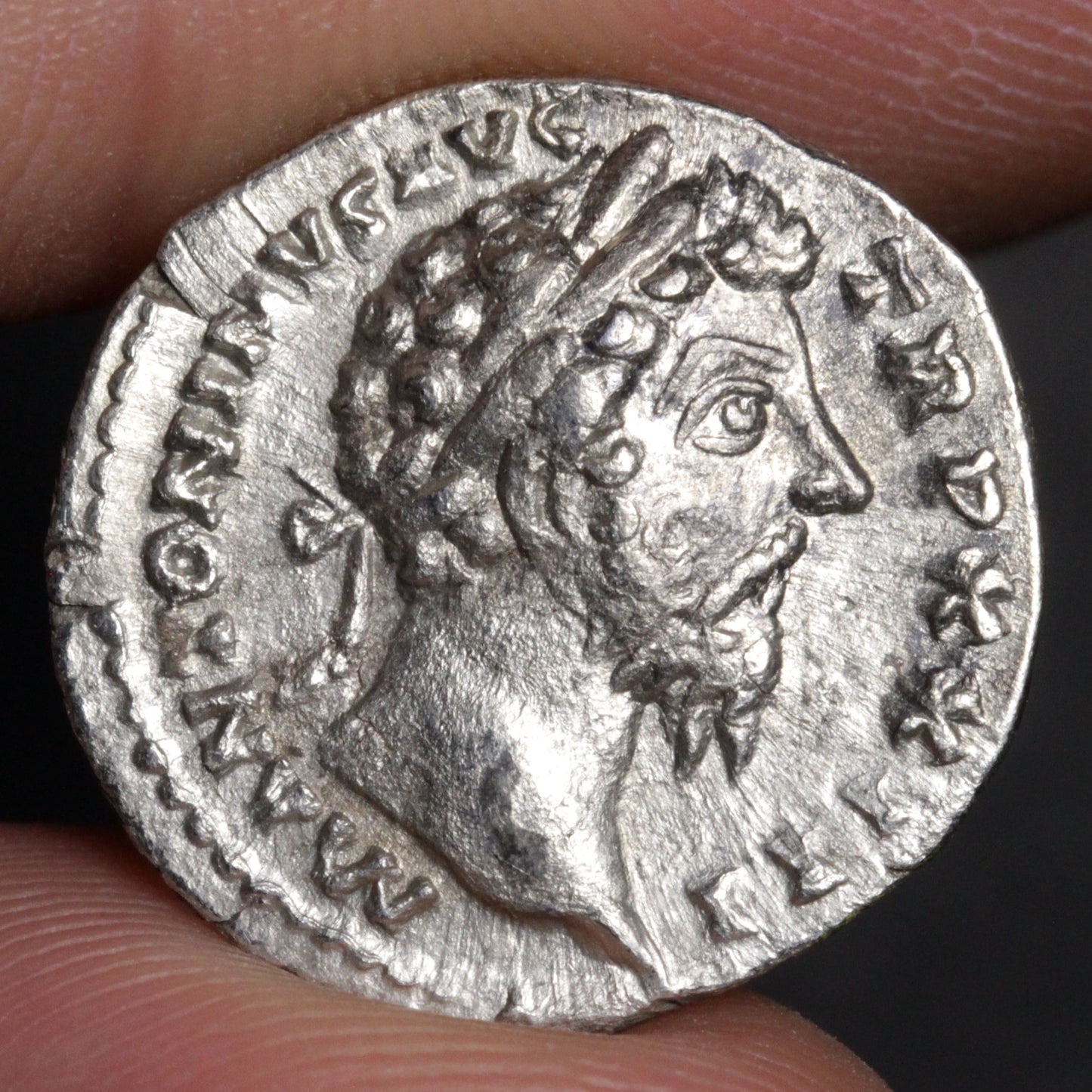 Ancient silver coin with a portrait of a Roman emperor held between fingers.