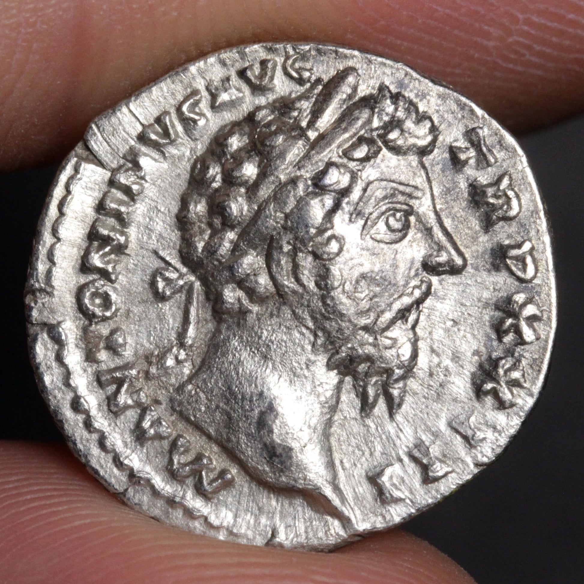 Ancient silver coin with a portrait of a Roman emperor held between fingers.