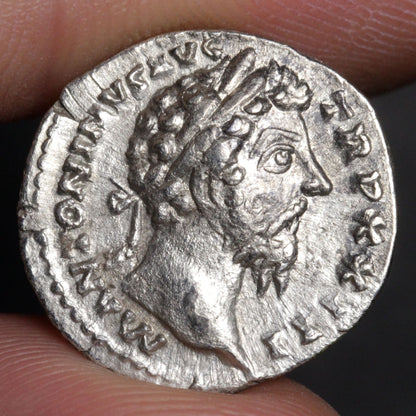 Ancient silver coin with a portrait of a Roman emperor held between fingers.