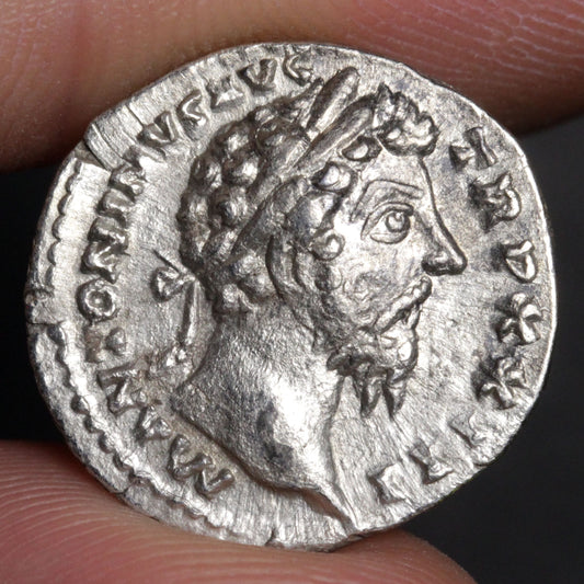 Ancient silver coin with a portrait of a Roman emperor held between fingers.