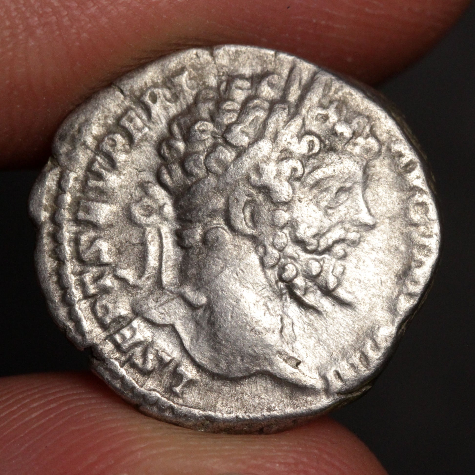 Ancient silver coin with a profile of a person held between fingers against a dark background