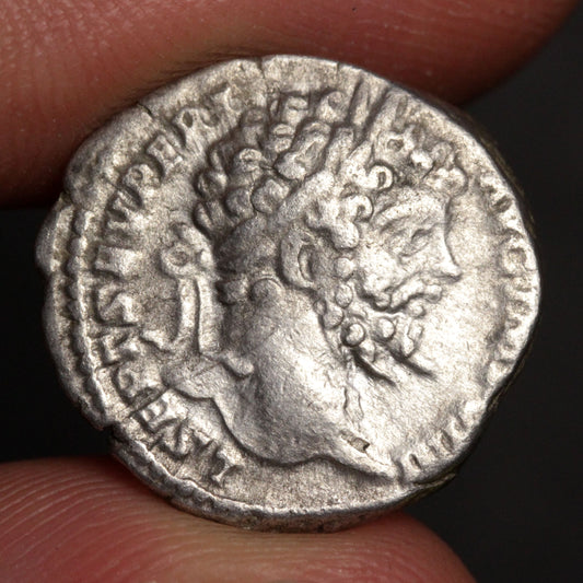 Ancient silver coin with a profile of a person held between fingers against a dark background