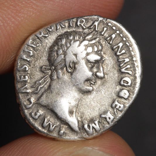 Ancient Roman silver coin held between fingers with dark background