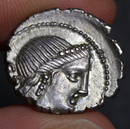 Ancient silver coin with a face design held between fingers against a dark background