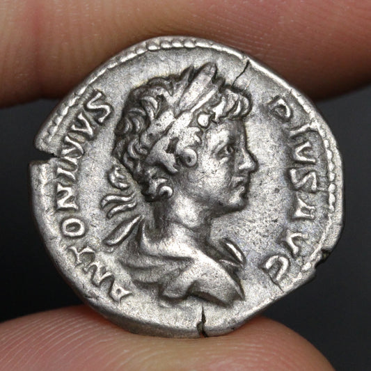 Ancient silver coin with profile of a bust held between fingers