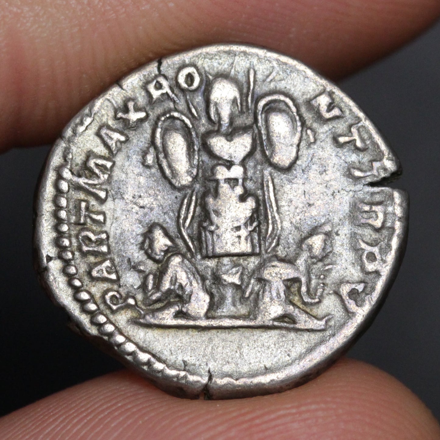 Ancient silver coin held between fingers with detailed design