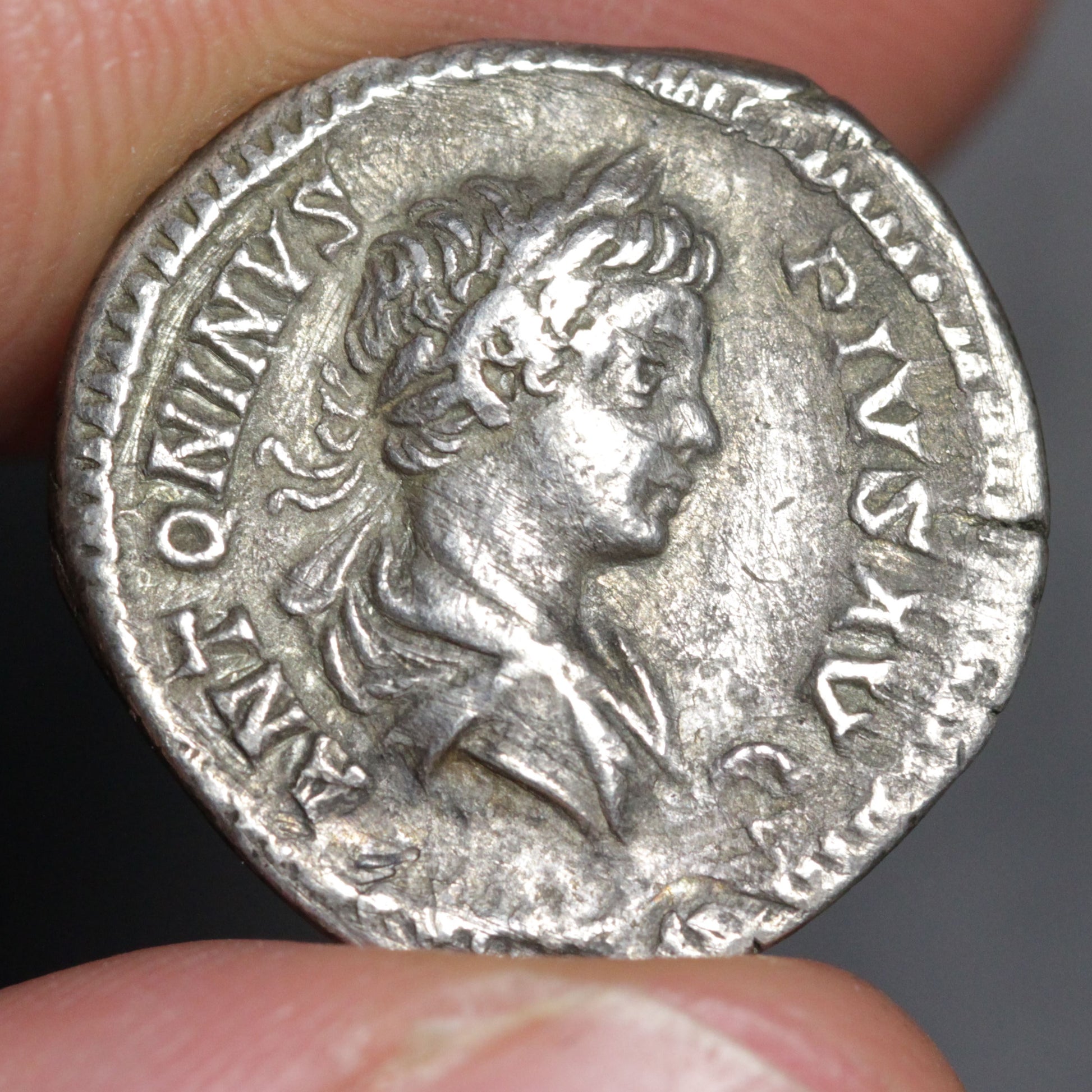 Ancient silver coin with profile of a person held between fingers