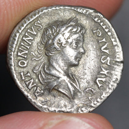 Ancient silver coin with profile of a person held between fingers