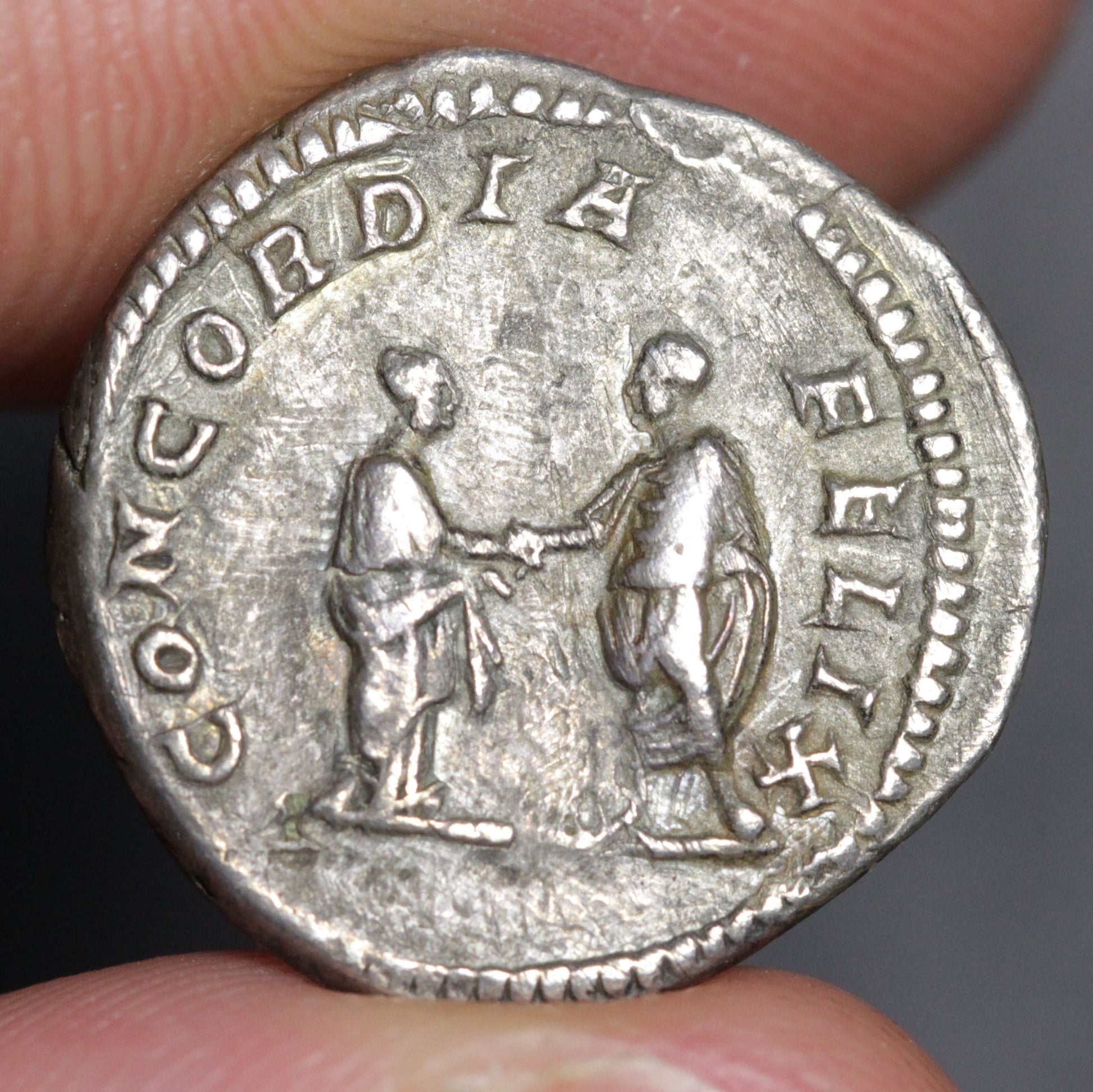 Silver coin with two figures shaking hands and engraved text held between fingers.