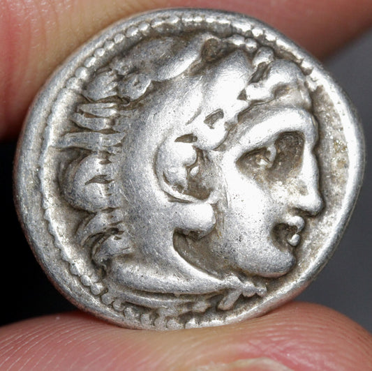 Silver coin with a profile of a person held between fingers
