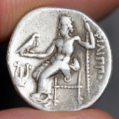 Ancient silver coin with a seated figure and inscriptions held between fingers