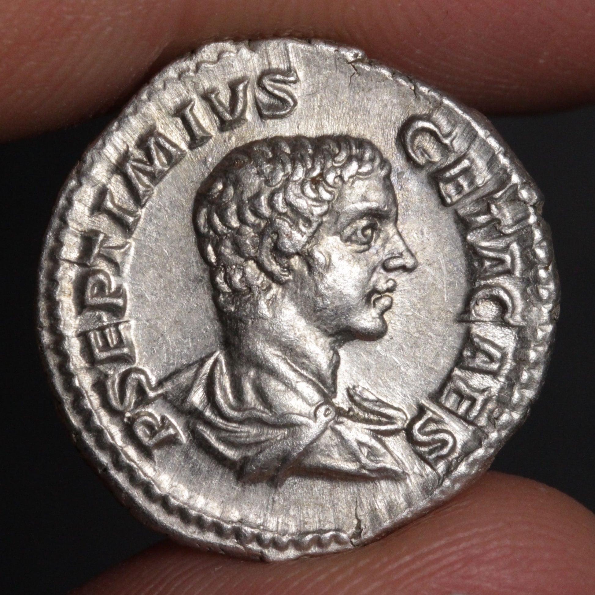 An ancient silver coin featuring a profile portrait of a Roman emperor, held between two fingers against a dark background.