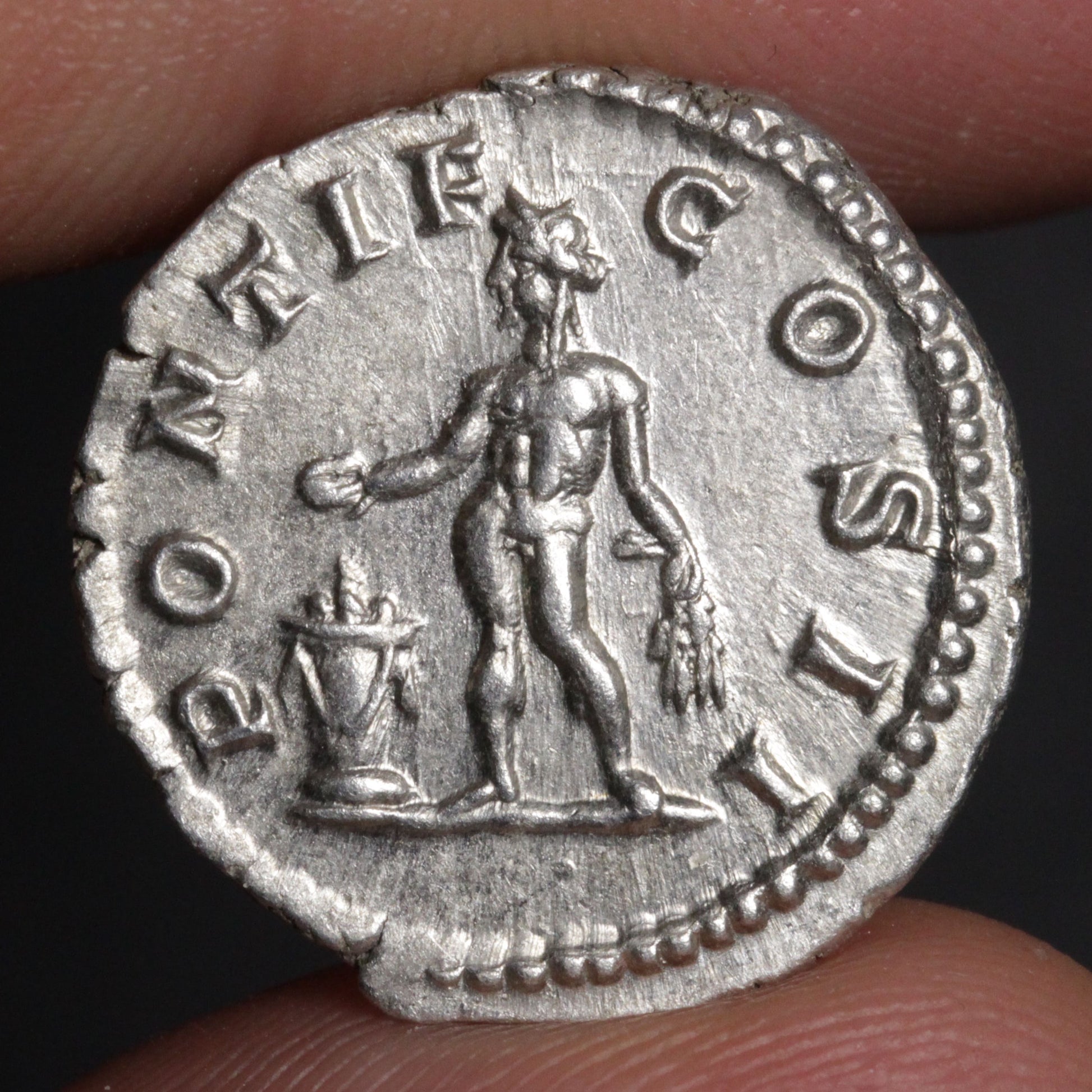 An ancient silver coin featuring a standing figure and the text 'PONTIF COS', held between fingers against a dark background.