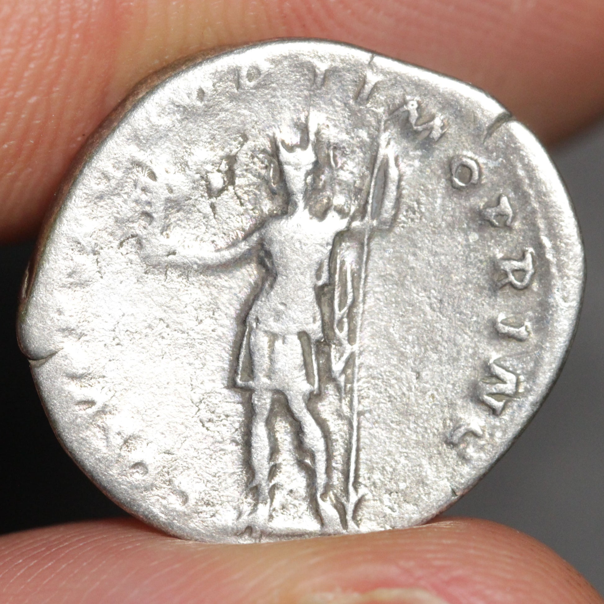 Silver coin with a figure and inscriptions held between fingers
