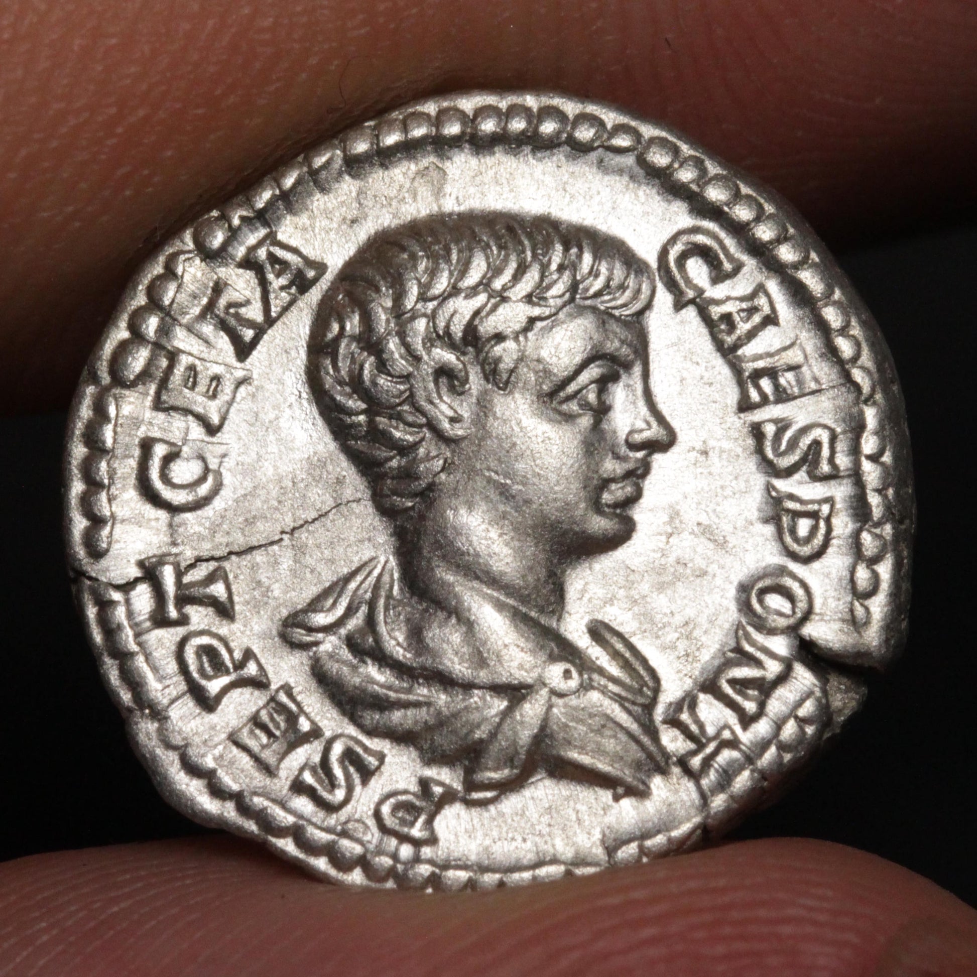 An ancient silver coin featuring a profile portrait of Geta, held between two fingers against a dark background.