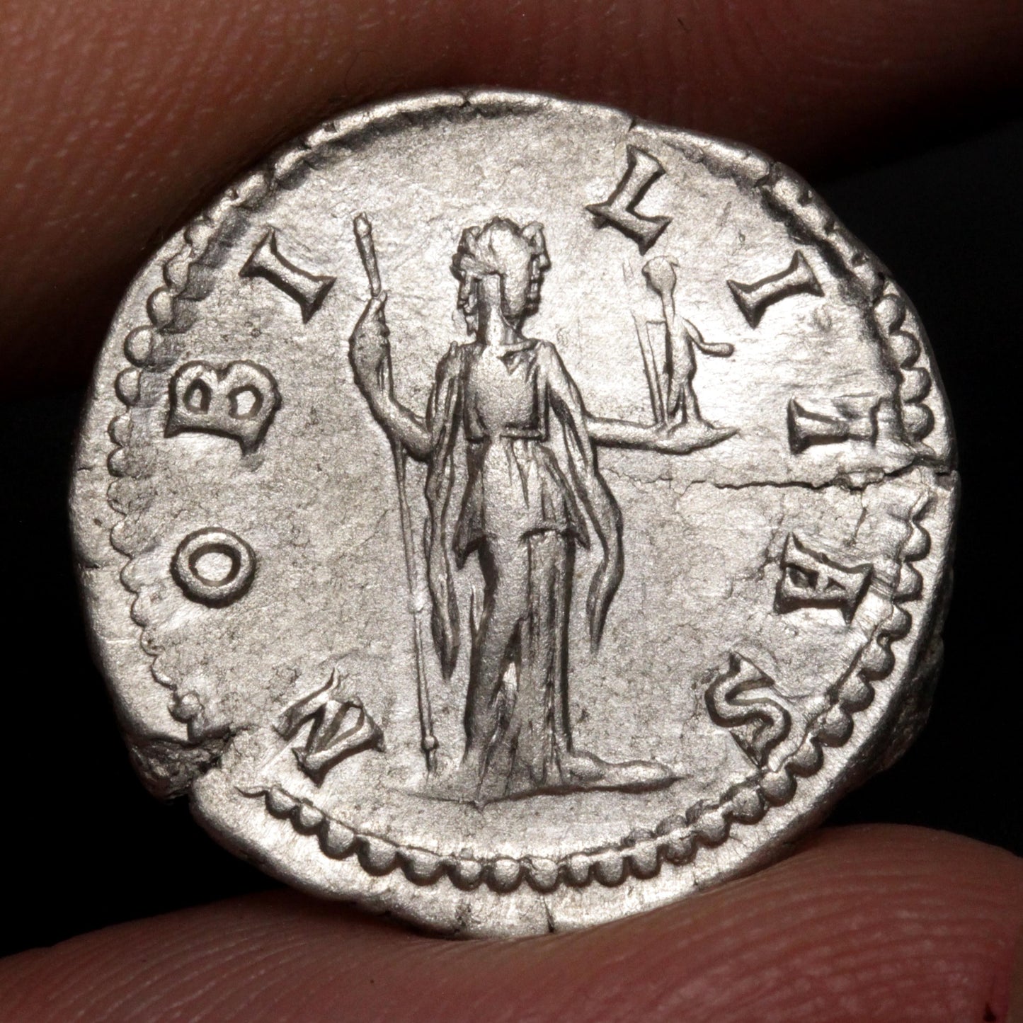 An ancient silver coin featuring a standing figure with outstretched arms, held between fingers against a dark background.