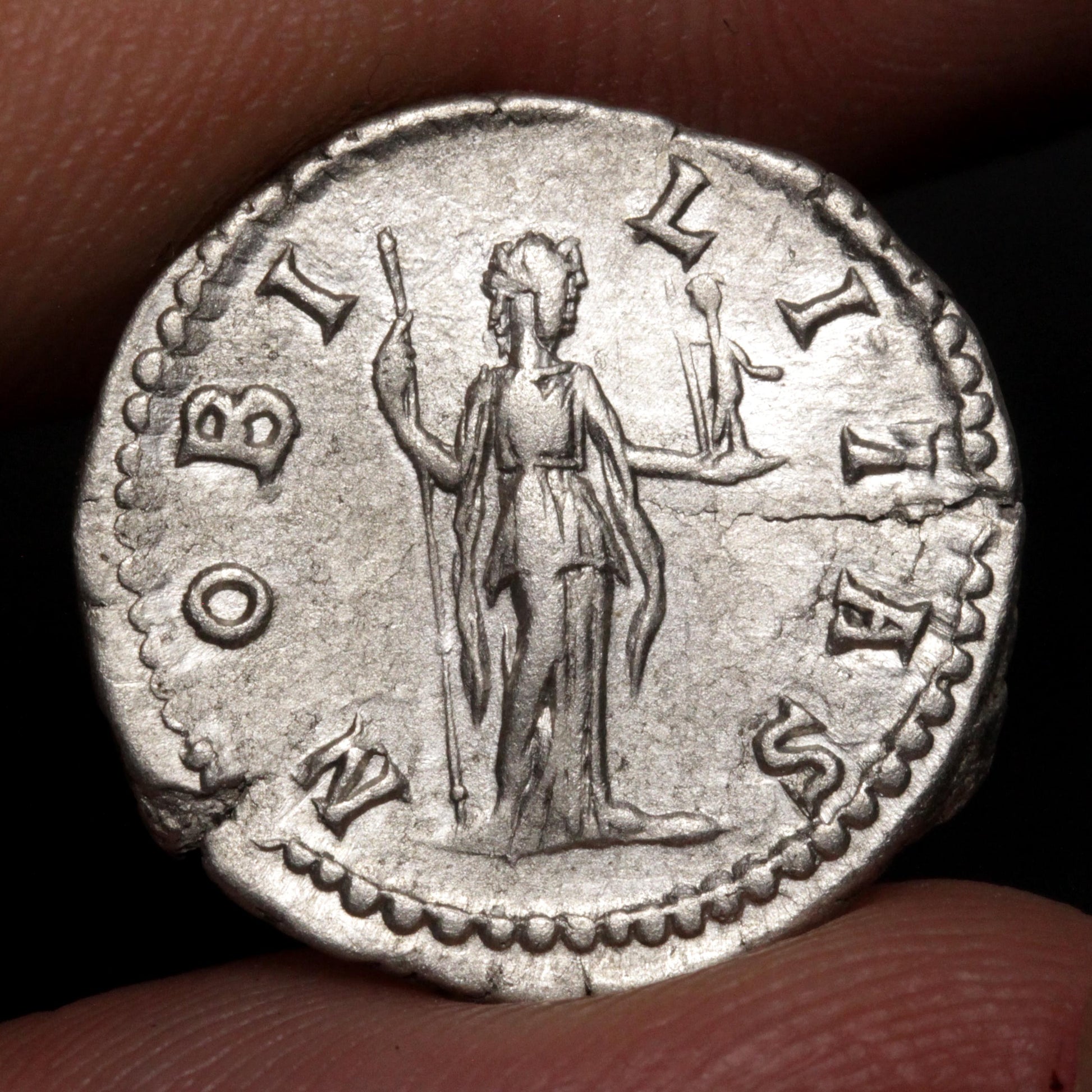 An ancient silver coin featuring a standing figure with outstretched arms, held between fingers against a dark background.